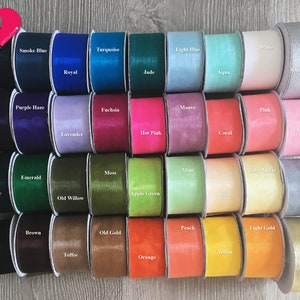 May include: A collection of 40 spools of ribbon in various colors, including black, white, red, green, blue, and yellow. The ribbon is arranged in rows of four, with each spool labeled with its color name.