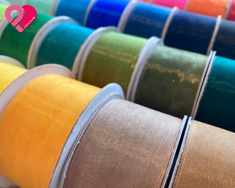 May include: A collection of spools of shimmering ribbon in various colors, including yellow, green, brown, and blue. The ribbon is made of a sheer, delicate fabric with a subtle sparkle.