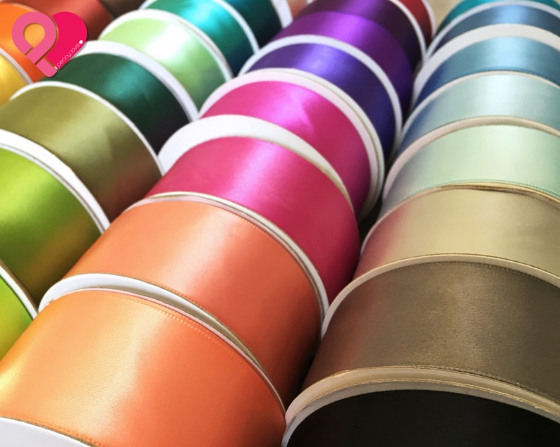 May include: A collection of colorful satin ribbon spools. The ribbons are in various shades, including orange, pink, green, and blue. The spools are neatly stacked, showcasing the glossy texture of the ribbon.