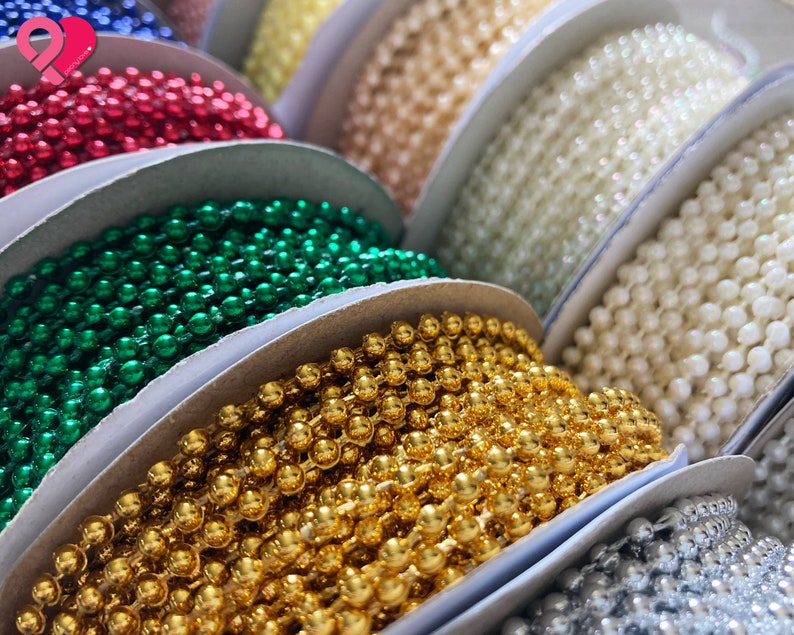 K&ouml;nnte beinhalten: Sortiment an Spulen mit bunten Perlen, darunter rot, gr&uuml;n, gold, wei&szlig; und silber. Die Perlen sind kreisf&ouml;rmig auf einer wei&szlig;en Oberfl&auml;che angeordnet.