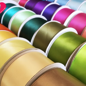 May include: A close-up of several spools of satin ribbon in various colors, including orange, yellow, green, and purple. The ribbon is neatly rolled on white cardboard spools, creating a visually appealing display. The image showcases a range of vibrant hues.