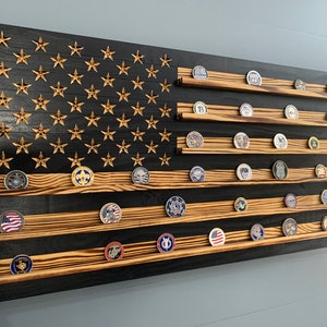 May include: A wooden American flag with a black and brown wood grain finish. The flag has 13 horizontal stripes and 50 stars. There are shelves on the flag to display challenge coins.