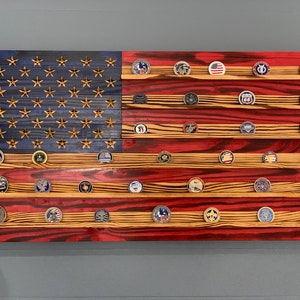May include: A wooden American flag with red, white, and blue paint, featuring a display of round, metal challenge coins on shelves.
