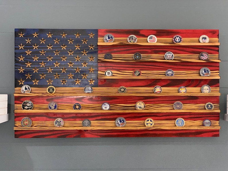 May include: A wooden American flag with red, white, and blue paint, featuring a display of round, metal challenge coins on shelves.