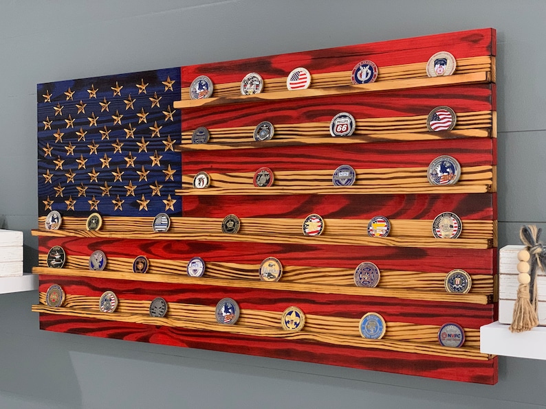 May include: A wooden American flag with red, white, and blue stripes. The flag has a blue field with white stars and is designed to hold challenge coins. The flag is made of reclaimed wood and has a distressed finish.