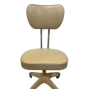 May include: Cream-colored vintage office chair with a rounded back and seat. The chair has a chrome frame and legs with rolling casters. The back is supported by two chrome bars. A classic piece of furniture.