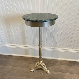 May include: A small, round side table with a green speckled top and a silver-colored metal base. The base has a decorative, ornate design with three feet. The table is approximately 24 inches tall.