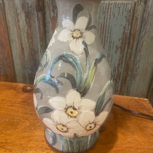 May include: A ceramic table lamp with a gray base and white floral design. The lamp features a stylized floral pattern with white flowers and green leaves.