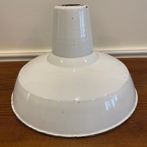 May include: White enamel industrial pendant light shade with a black rim. The shade has a slightly domed shape and a small opening at the top.