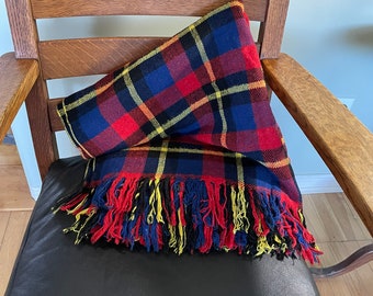 May include: A red, blue, and yellow plaid throw blanket with fringe on a wooden chair with a black leather seat.