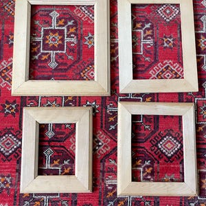 May include: Four unfinished wooden picture frames of varying sizes. The frames are rectangular with a light wood grain. They are arranged on a red patterned rug with a geometric design. The frames are ready for artwork or photos.