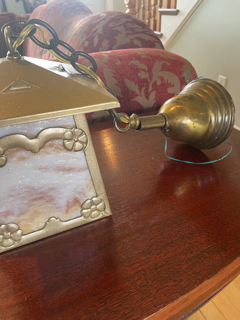 May include: A gold and white stained glass ceiling light fixture with a brass chain and a brass bell-shaped canopy.