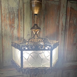 May include: A vintage brass and glass ceiling light fixture with a geometric patterned glass shade. The fixture has a decorative, ornate design and is hanging from a chain.