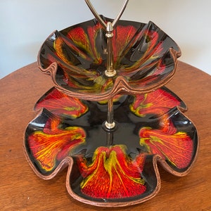 May include: Two-tiered serving tray with a black base and red, yellow, and orange swirl design. The tray has a metal handle and is ideal for serving snacks or desserts.