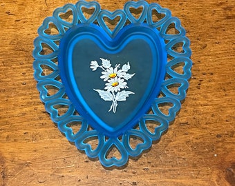 May include: A blue glass heart-shaped dish with a lace-like edge and a painted design of white daisies.
