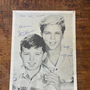 May include: A black and white photograph featuring two young boys with handwritten ink inscriptions. The text reads From your friends, Beaver Jerry Mathers, and Wally Tony Dow. The boys are wearing collared shirts, one plaid and one solid.