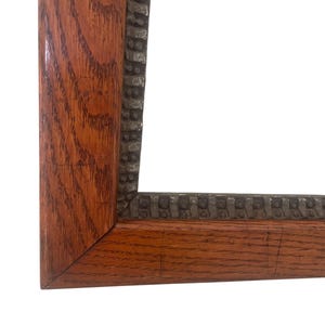 May include: A close-up of a corner of a wooden picture frame. The frame has a dark brown, textured wood grain with a decorative, dark metal trim. The frame is empty, with a white background.