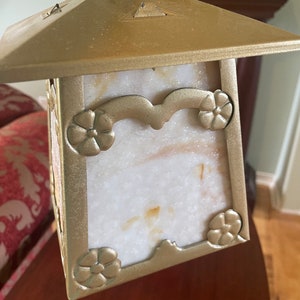 May include: A gold-toned pendant light fixture with a square, frosted glass shade. The shade has a decorative floral design around the edges and a white, marbled pattern.