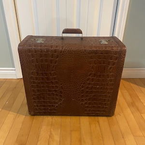 May include: A brown leather suitcase with a crocodile pattern. The suitcase has a metal handle and metal clasps.