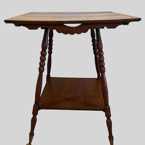 May include: A brown wooden side table featuring a rectangular top with a carved fan-shaped detail, a lower shelf, and four turned legs. The legs terminate in brass-colored metal claw-and-ball feet, providing a distinct finish to the furniture piece.