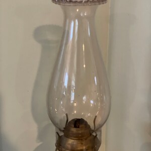 May include: A clear glass oil lamp with a frosted glass chimney and a metal burner. The chimney has a beaded rim.