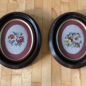 May include: Two antique oval frames with dark wood finishes and gold trim. Each frame contains a needlepoint embroidery of a floral bouquet with pink, yellow, and green flowers.