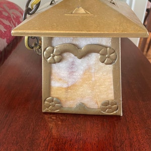 May include: A brass and glass pendant light fixture with a square, frosted glass shade. The shade has a decorative floral design around the edges. The fixture is hanging from a chain.
