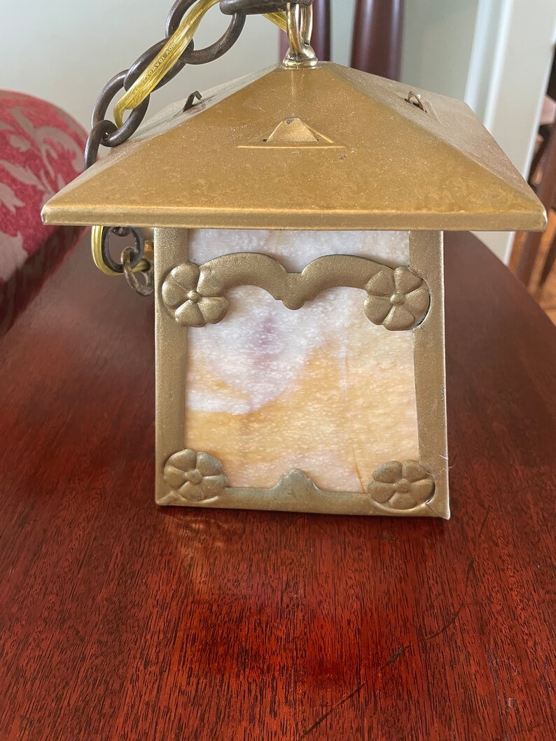 May include: A brass and glass pendant light fixture with a square, frosted glass shade. The shade has a decorative floral design around the edges. The fixture is hanging from a chain.