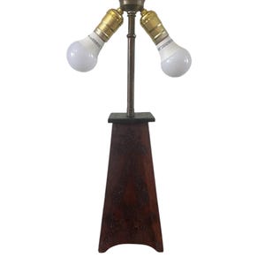 May include: A two-light table lamp with a brass base and a wooden pedestal. The lamp has a dark brown finish and a geometric pattern on the pedestal.