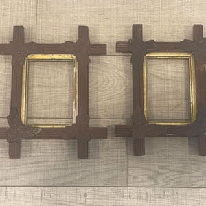 May include: Two rectangular picture frames constructed from dark brown wood with a ribbed texture. Each frame features four decorative dark brown leaf-shaped accents at the corners and a thin, metallic gold-colored inner border surrounding the opening.