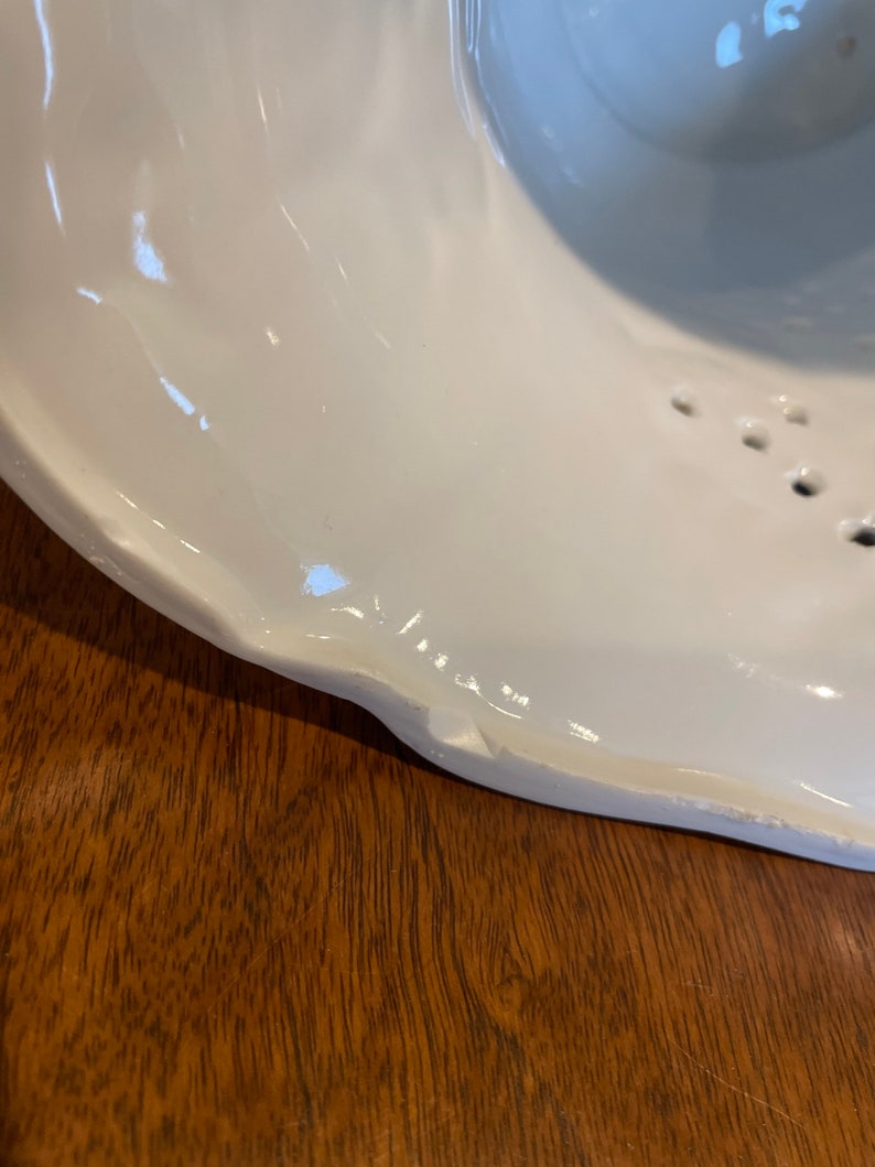 May include: White ceramic bowl with a chipped edge. The bowl has a textured surface and a series of small holes around the rim.