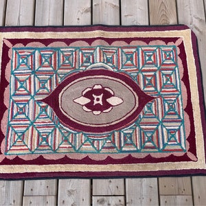 May include: A vintage hooked rug with a geometric pattern in shades of red, blue, green, and beige. The rug features a central oval with a floral design.