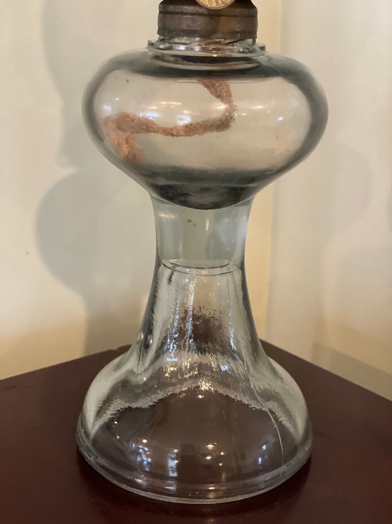 May include: A clear glass oil lamp with a round, bulbous top and a wide, flared base. The lamp has a metal wick holder and a metal cap on top.