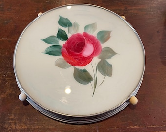 May include: A white glass cake stand with a silver rim and four ivory knobs. The glass features a hand-painted red rose with green leaves.