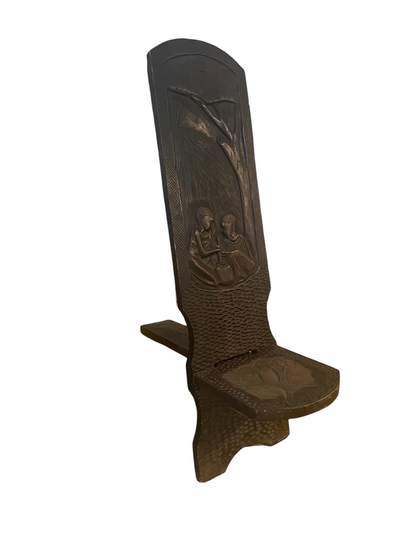 May include: A dark brown wooden chair with a carved design of two people sitting under a tree. The chair has a simple, rustic design and is made of solid wood.