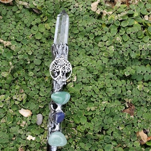 May include: A silver wand with a clear crystal point, a silver tree of life charm, and green and blue gemstone accents.