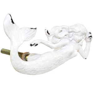 May include: White mermaid cabinet knob with black accents. The mermaid is in a reclining pose with flowing hair and a fishtail. The knob is attached to a threaded rod with a nut and washer.