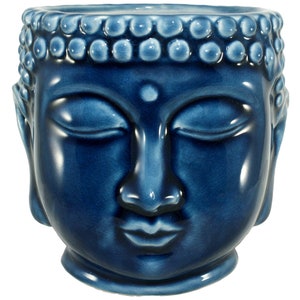 May include: A blue ceramic planter shaped like the face of Buddha. The planter has a smooth, glazed finish and features closed eyes, a small dot on the forehead, and a serene expression.
