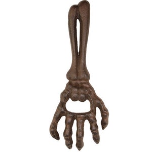 May include: A cast iron bottle opener shaped like a skeletal hand with a rusty brown finish.