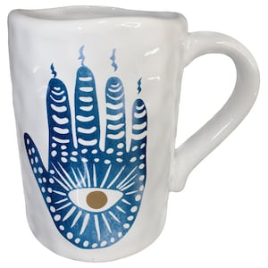 May include: White ceramic mug with a blue and white hamsa hand design. The hamsa hand has a gold eye in the center.