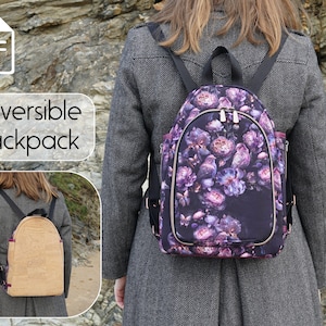 May include: A reversible backpack with a floral print on one side and a cork fabric on the other side. The backpack is being worn by a person standing in front of a rocky background.