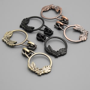 May include: Four zipper pulls with floral designs. The pulls are in gold, silver, and black metal.