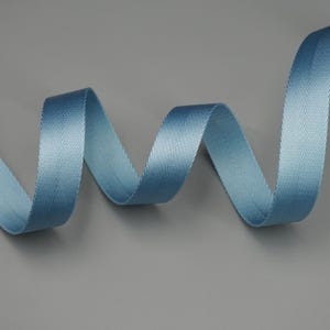 Peut inclure: Un ruban bleu clair en chevrons, gracieusement courb&eacute; sur un fond gris. La texture du ruban est finement tiss&eacute;e, avec un l&eacute;ger &eacute;clat. Le motif pr&eacute;sente un motif en chevrons classique, id&eacute;al pour les travaux manuels et d&eacute;coratifs.