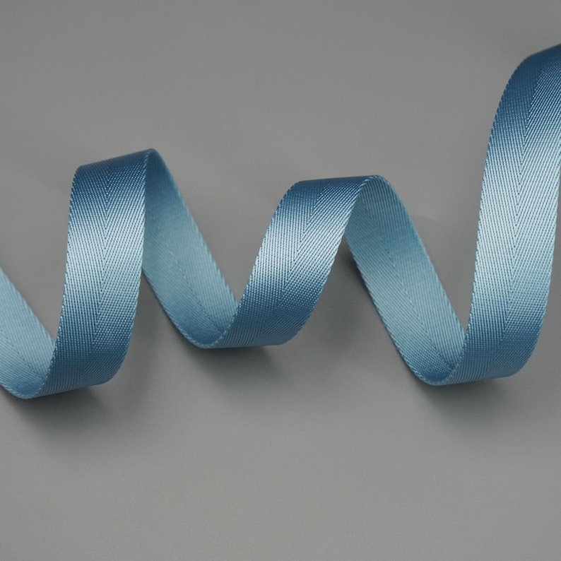 Peut inclure: Un ruban bleu clair en chevrons, gracieusement courb&eacute; sur un fond gris. La texture du ruban est finement tiss&eacute;e, avec un l&eacute;ger &eacute;clat. Le motif pr&eacute;sente un motif en chevrons classique, id&eacute;al pour les travaux manuels et d&eacute;coratifs.