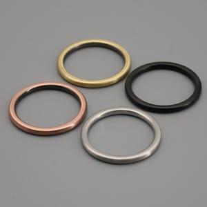 May include: Four metal rings in different colours: gold, copper, black and silver. The rings are all the same size and shape, and they are arranged in a row.