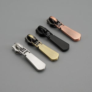 Puede incluir: Cuatro tiradores de cremallera en diferentes acabados: plata, oro, negro y cobre. Cada tirador tiene un diseño único y está hecho de metal.