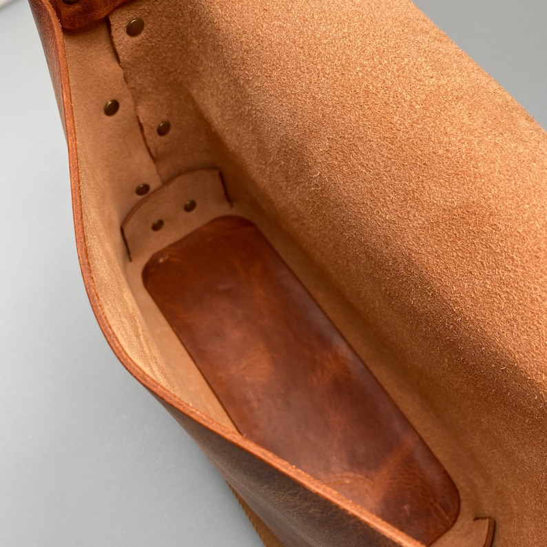 May include: The inside of a brown leather bag with a suede lining. The bag has a flap closure and is secured with metal snaps.