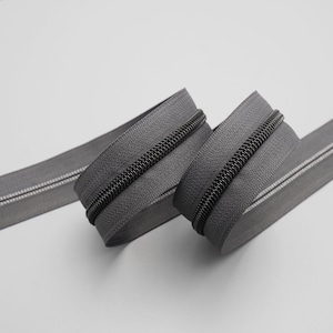May include: Two rolls of black zipper tape with a silver zipper pull. The zipper tape is coiled and the zipper pull is visible.