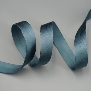 Peut inclure: Un ruban en chevrons de couleur teal, joliment courb&eacute; sur un fond neutre. La texture et le l&eacute;ger &eacute;clat du ruban sont visibles, soulignant son potentiel d&eacute;coratif. Id&eacute;al pour l'artisanat, la couture ou pour ajouter une touche raffin&eacute;e aux cadeaux.