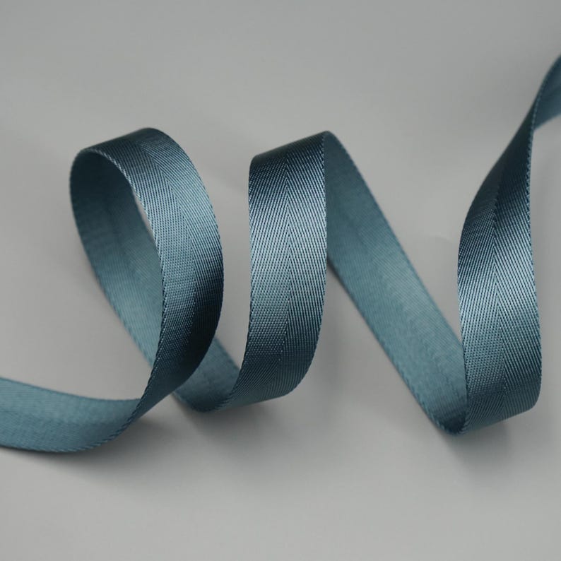 Peut inclure: Un ruban en chevrons de couleur teal, joliment courb&eacute; sur un fond neutre. La texture et le l&eacute;ger &eacute;clat du ruban sont visibles, soulignant son potentiel d&eacute;coratif. Id&eacute;al pour l'artisanat, la couture ou pour ajouter une touche raffin&eacute;e aux cadeaux.